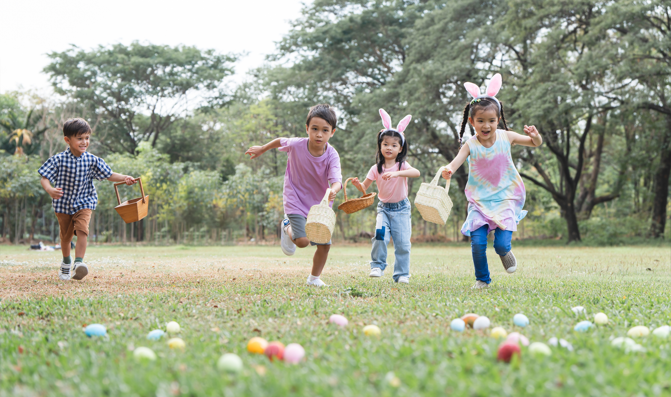 Happy group of cute little children hunting Easter eggs, wearing bunny ears. kids holding basket, running to collect eggs on grass while playing outdoors at park