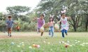 Happy group of cute little children hunting Easter eggs, wearing bunny ears. kids holding basket, running to collect eggs on grass while playing outdoors at park
