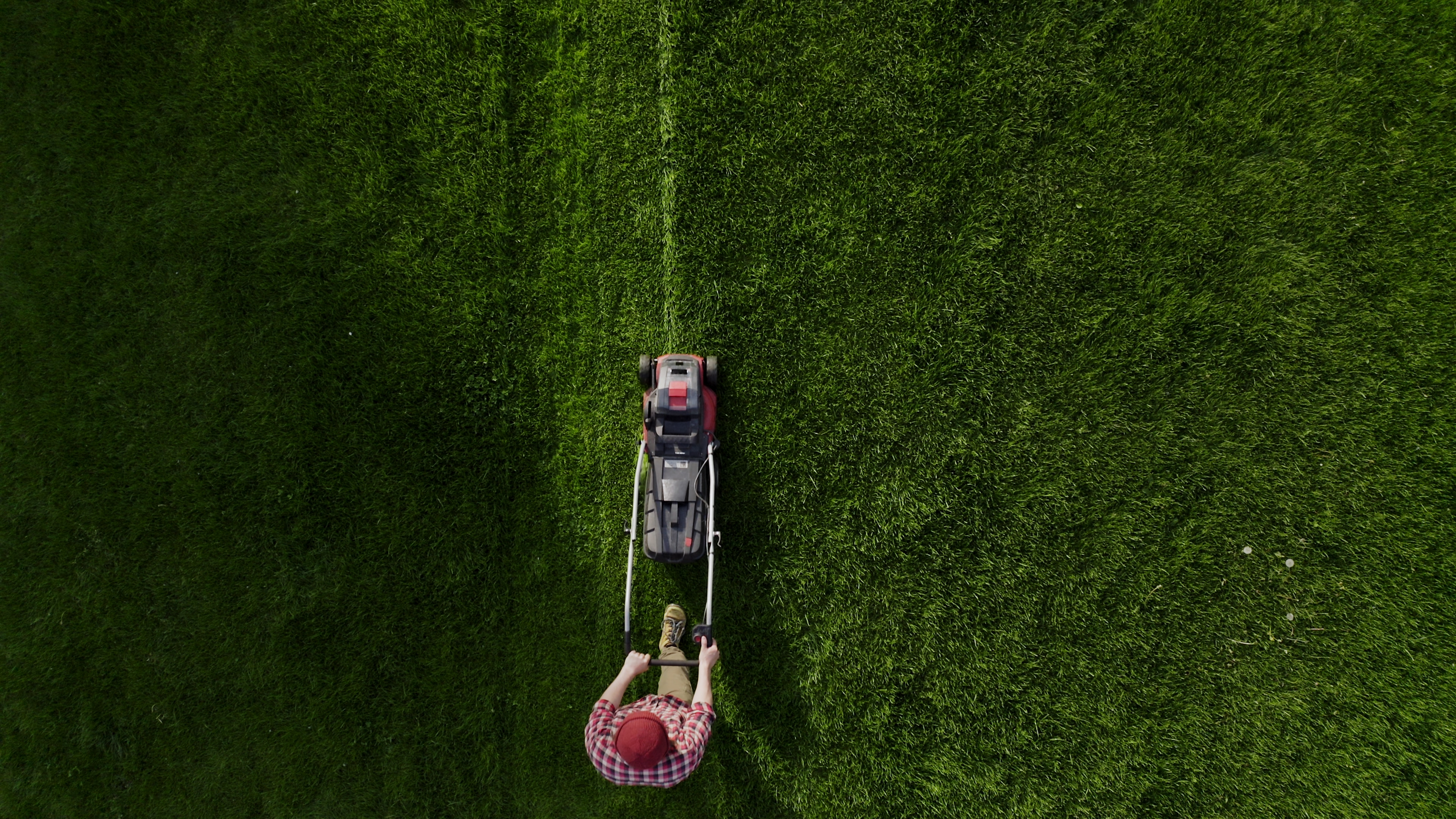 Top view of the lawn-mover worker cutting green grass garden. Unknown man worker cutting grass with lawn mower above view