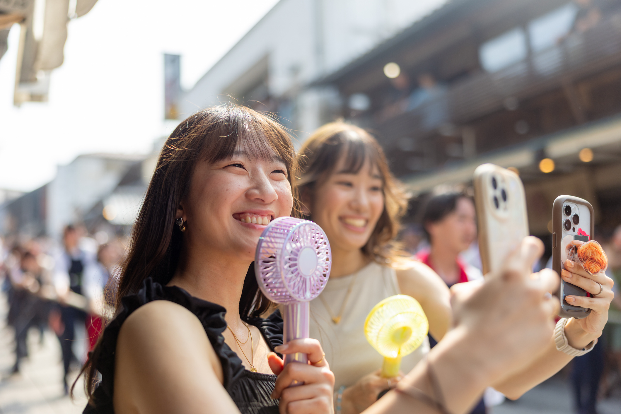 Young female friends using handheld fans while taking photos at a festival