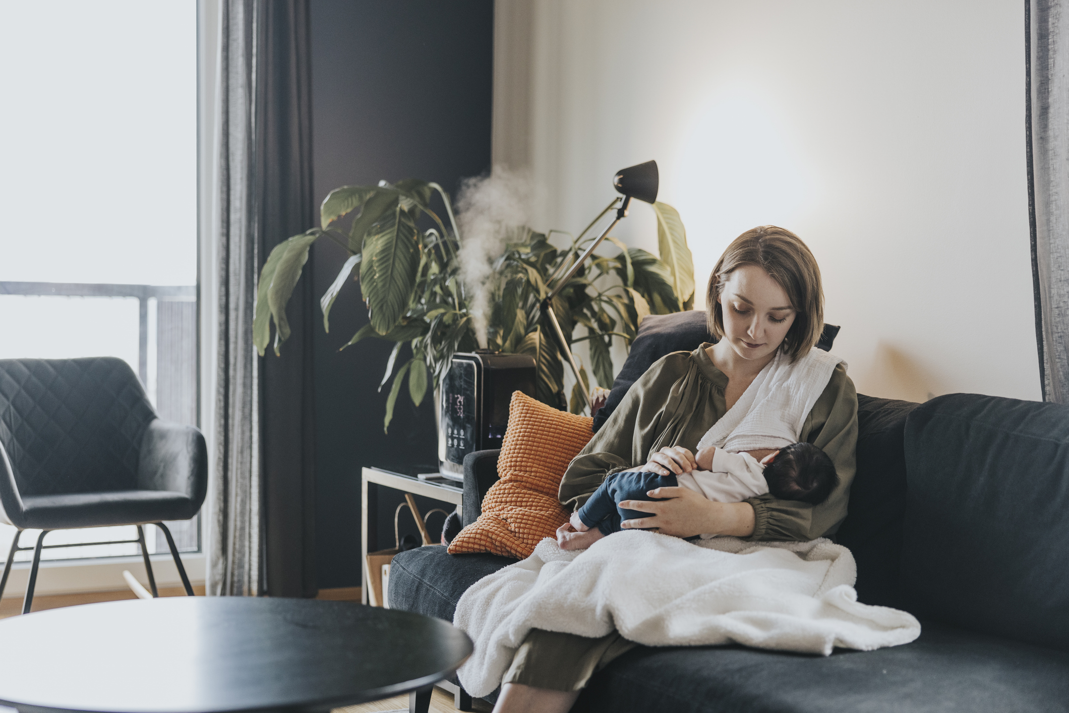 Young Caucasian mother breastfeeding her newborn baby girl at home.
