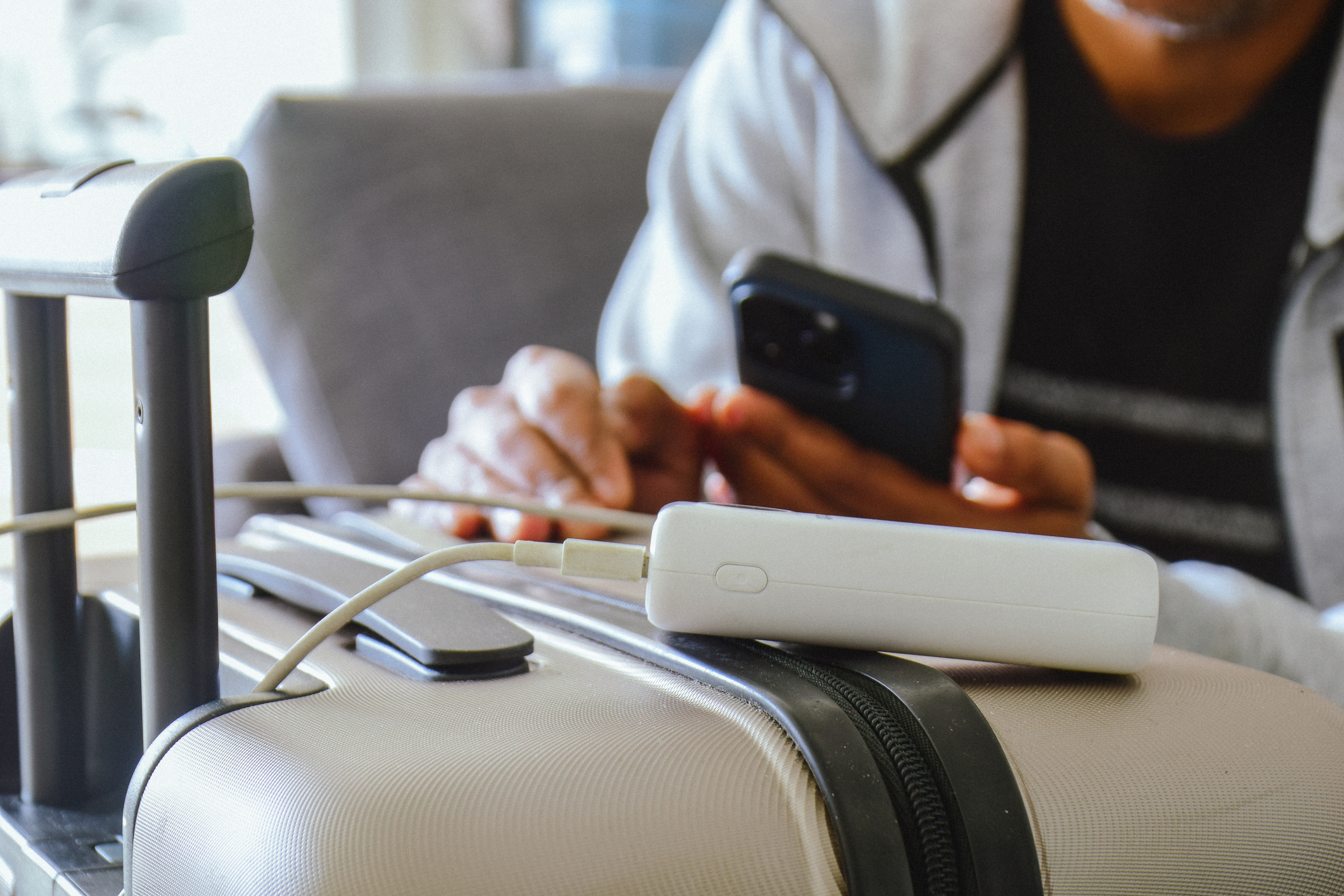 Cropped image of a South Asian man waiting in airport lounge charging his phone using power banks under $50 before departure. Focus on the foreground.