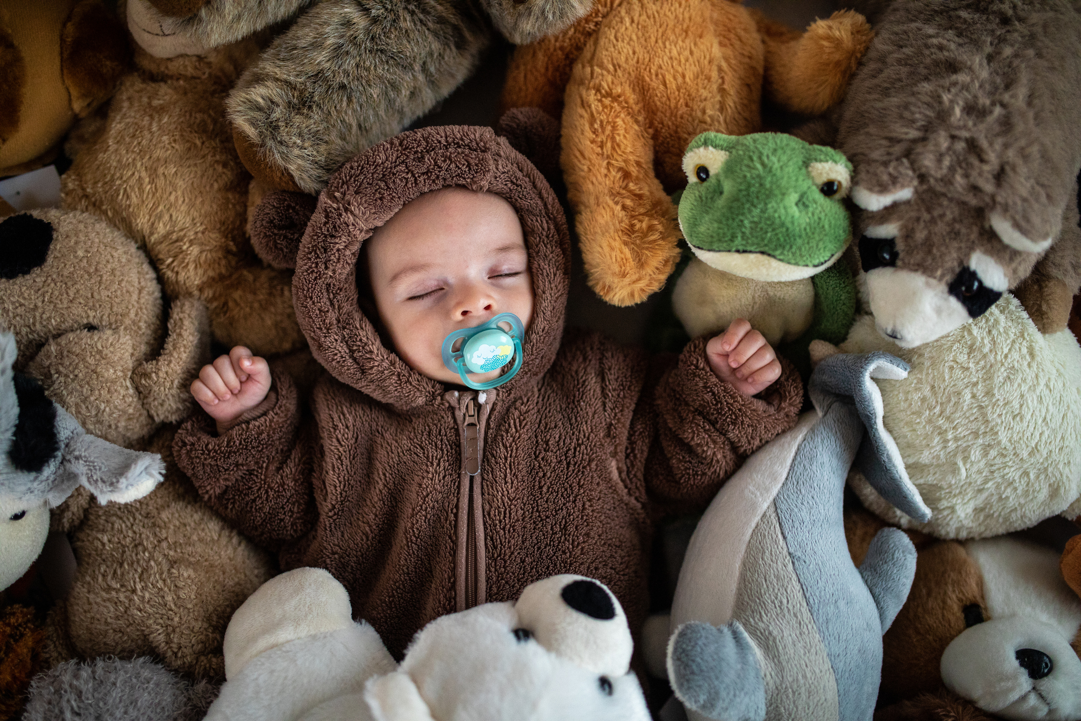 Sleeping little baby in warm baby clothing taking a nap between heap of soft toys