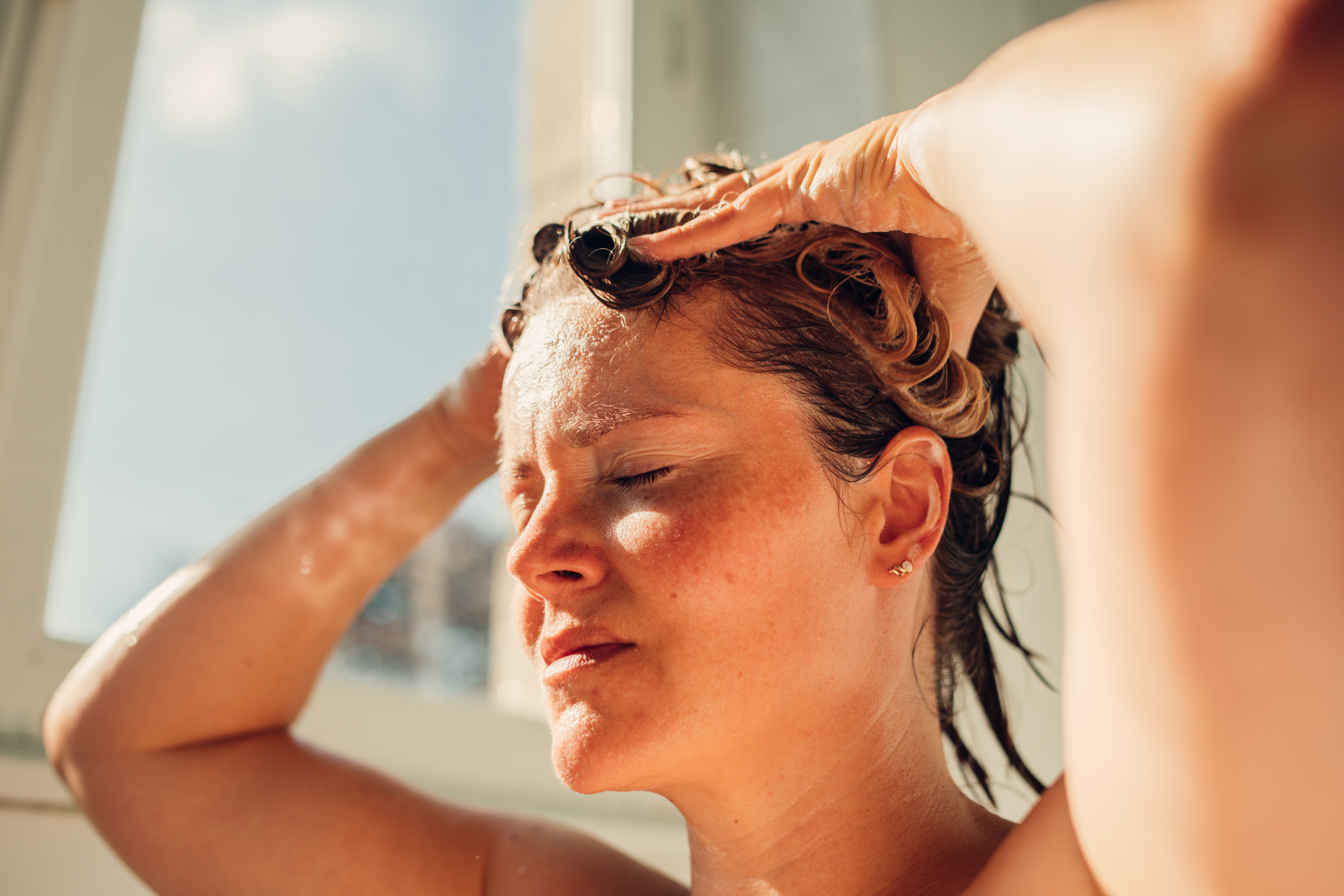 Woman washing hair with products from the Sol de Janeiro BSS sale at a bright sunny day.