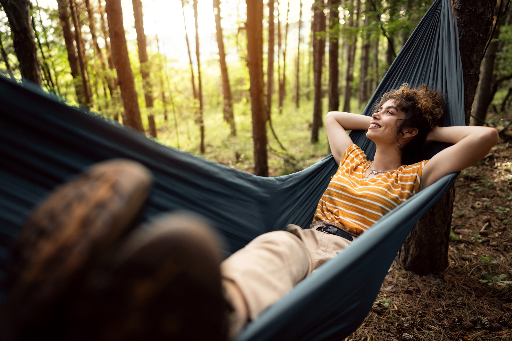 Cheerful young Caucasian female hiker resting in a hammock in the pine forest.