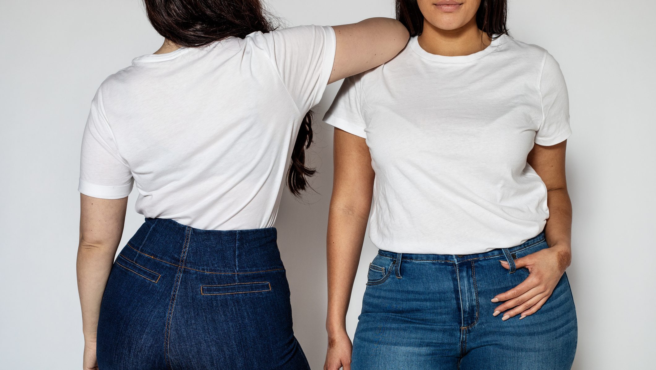Cropped shot of two women standing in opposite directions on white background. Women wearing white t-shirt and blue denim jeans.