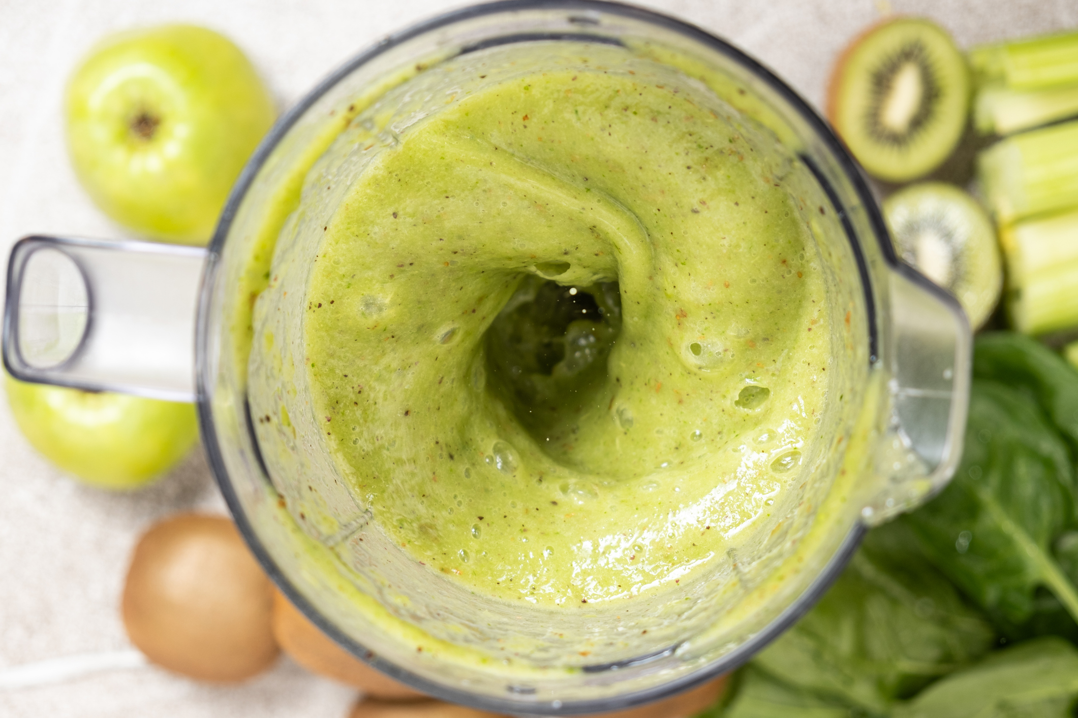 Making a green smoothie with celery, kiwi, apple and spinach in a blender, top view