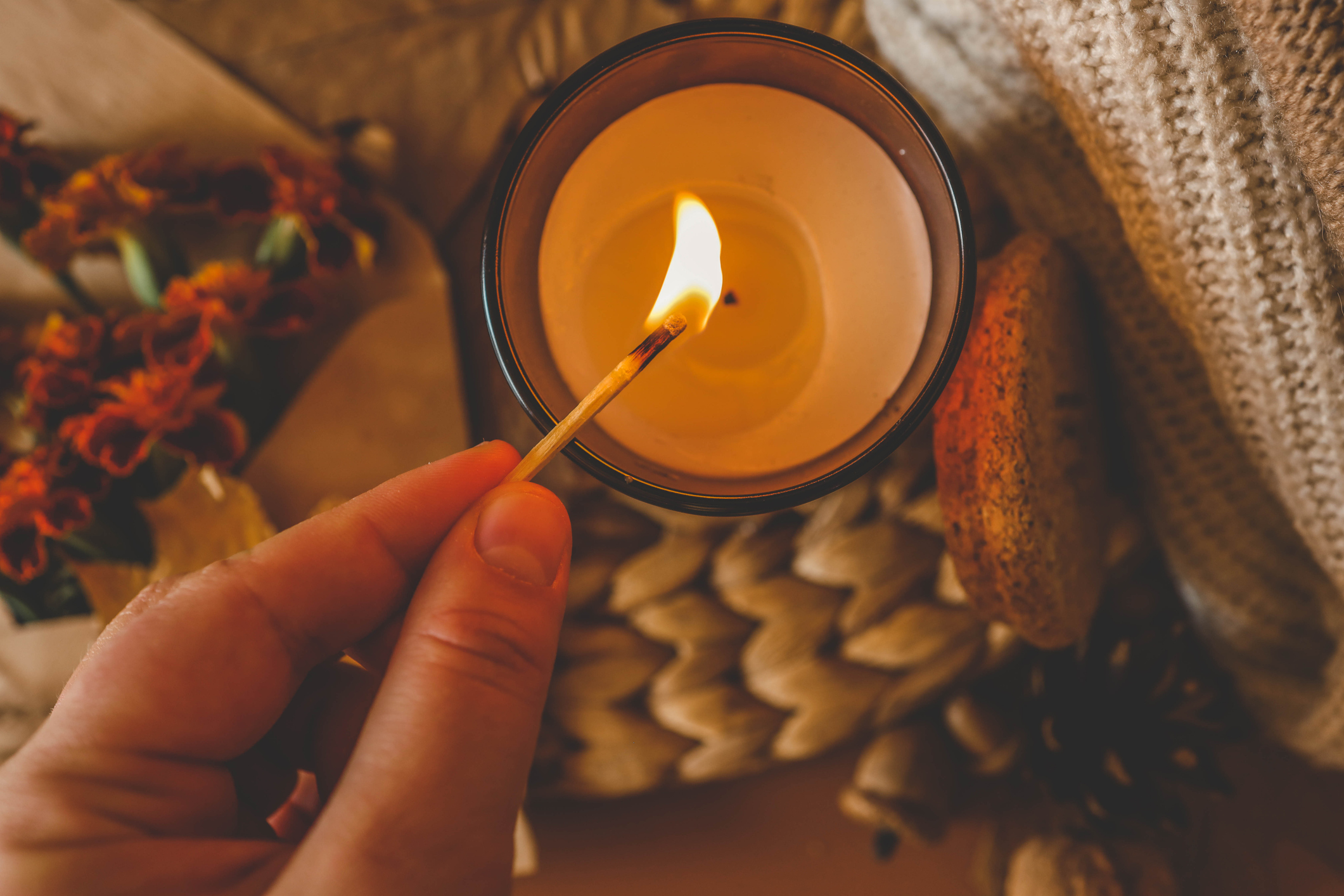Close-up of a hand lighting a red candle with a match, creating a warm and cozy atmosphere.