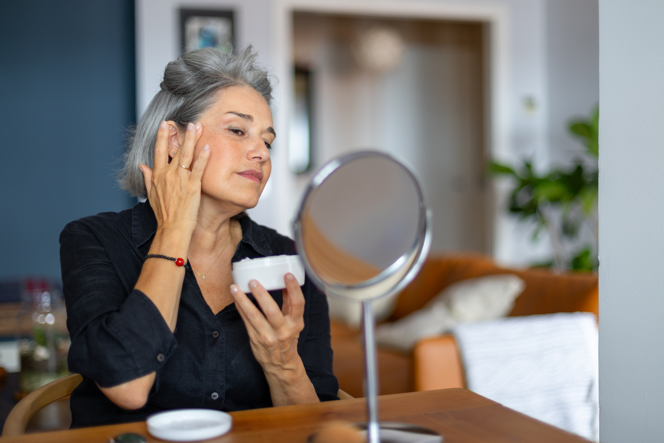 Mature woman taking care of her skin, applying anti aging cream while looking in a small mirror
