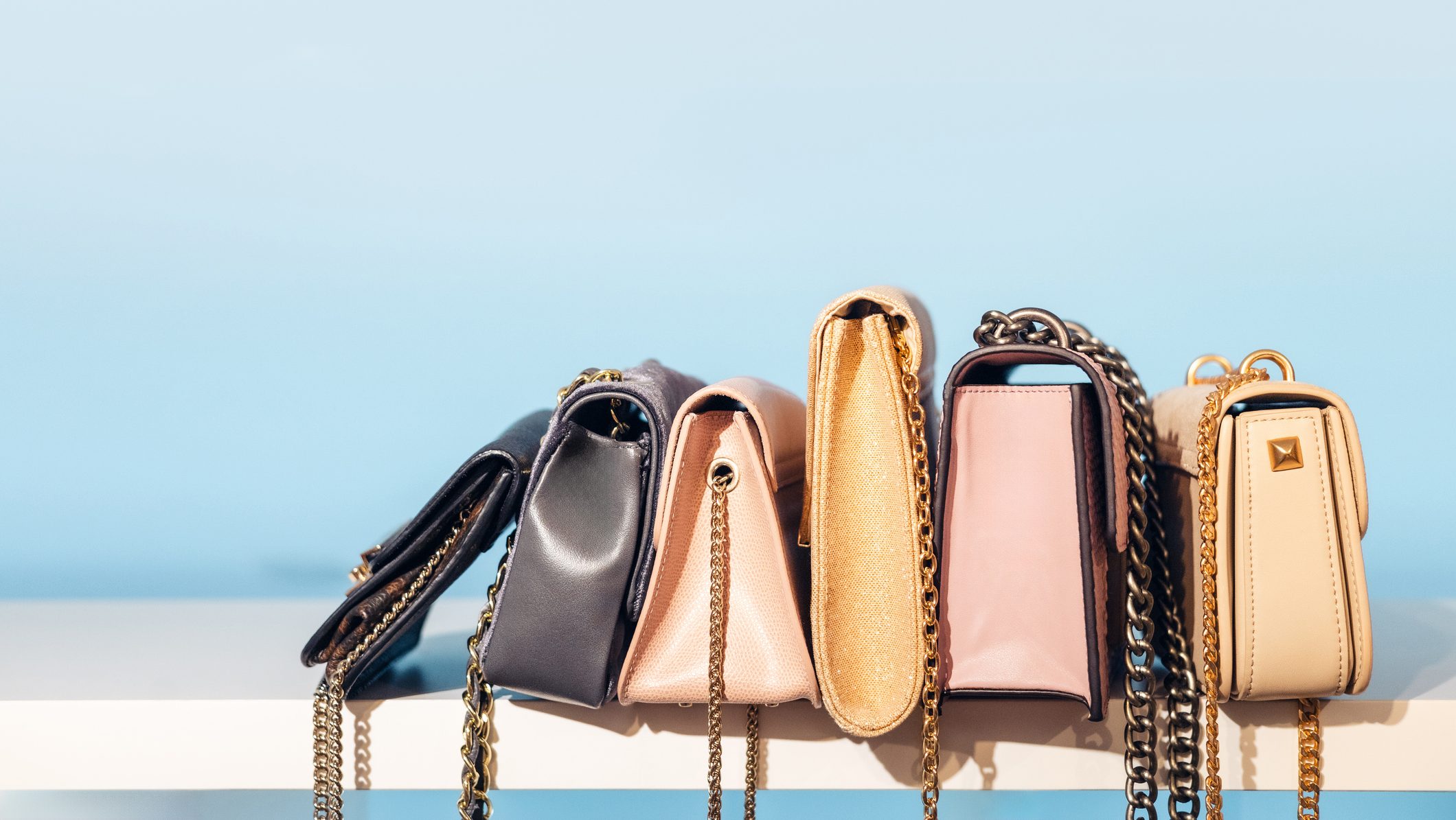 Row of small handbags arranged on white shelf against pastel wall