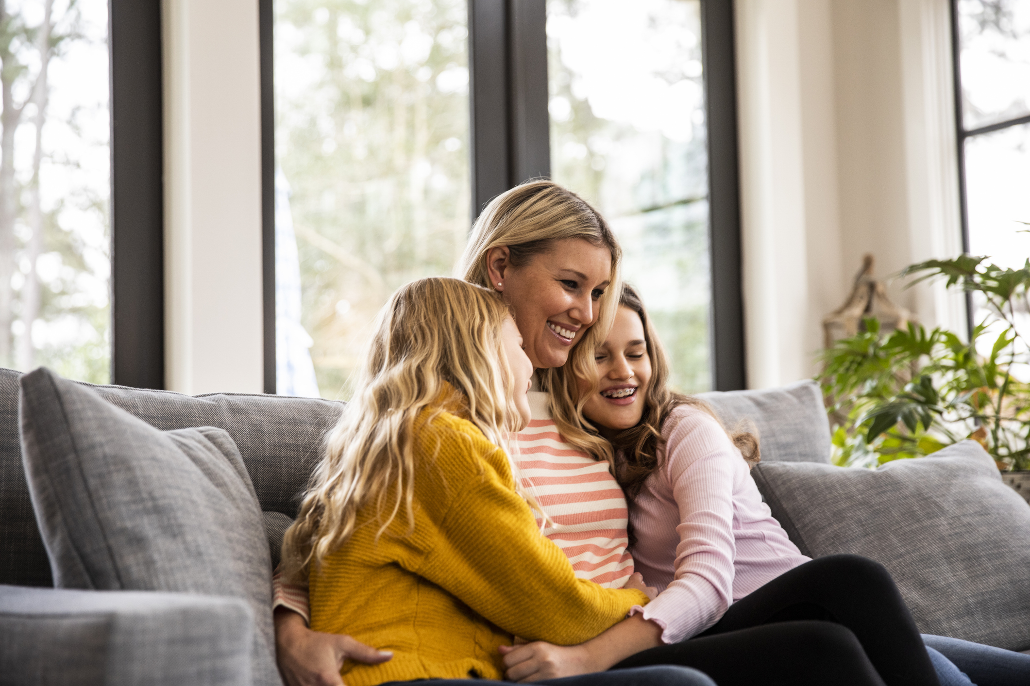 Mother and tween daughters embracing on couch in modern home