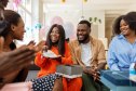 Young pregnant woman getting baby clothes as a present from her friends at a baby shower party at her home. Pregnant woman opening presents and showing them to friends sitting by during her baby shower party.