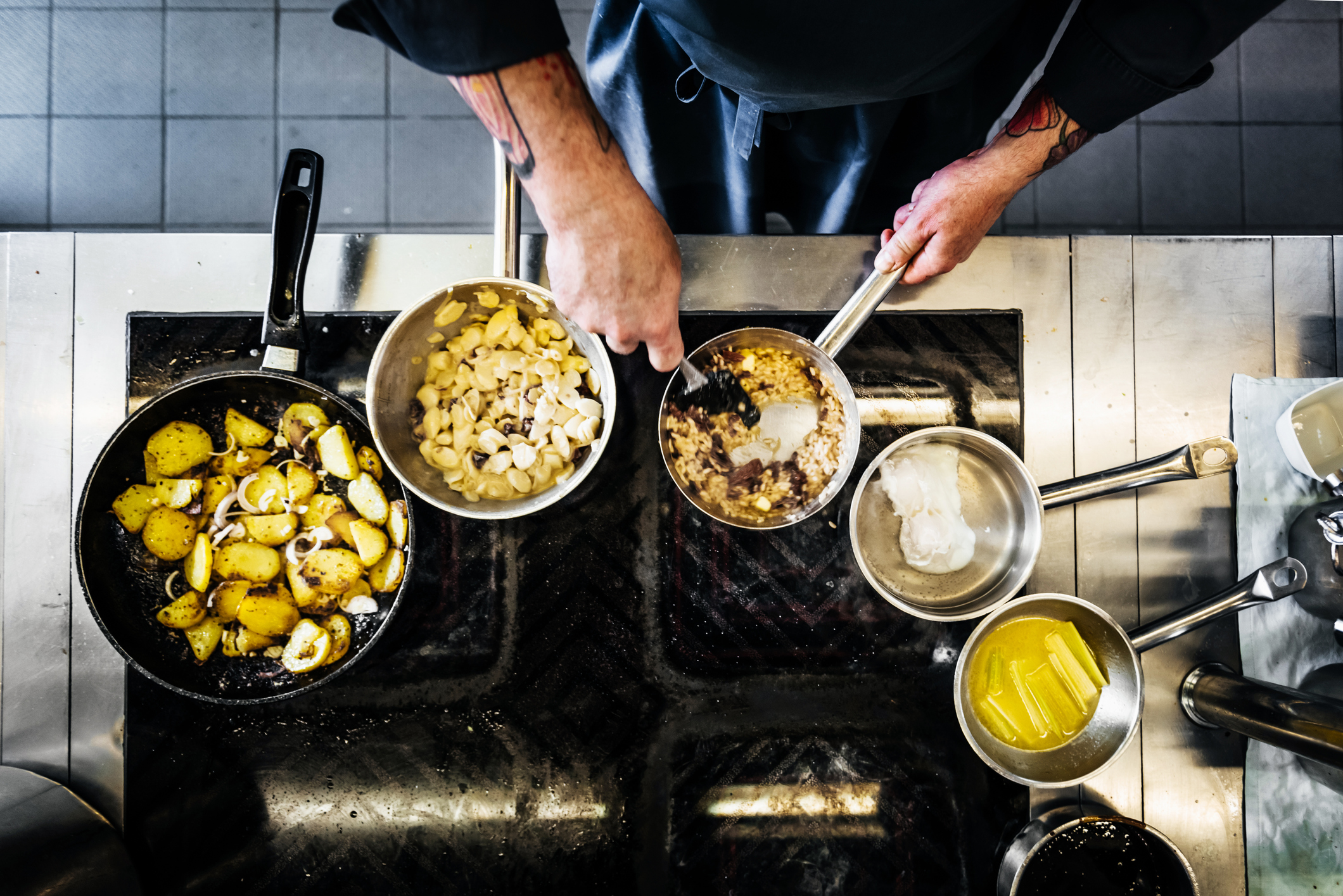 An aerial shot of a chef cooking with several pans on the hob in his restaurant kitchen.