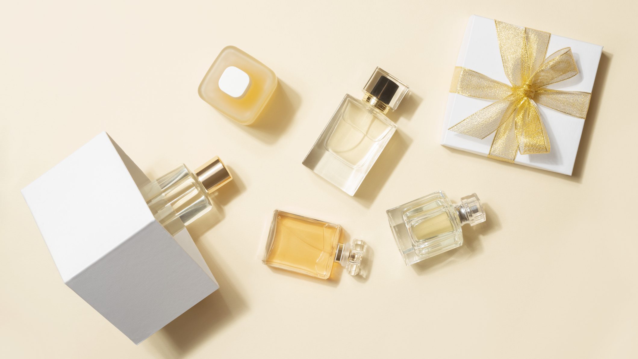 Many perfume bottles and gift box flat lay on light beige background