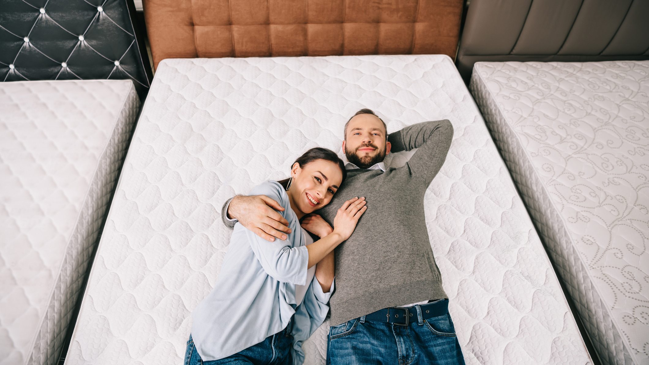 overhead view of smiling couple lying on bed in furniture store with arranged mattresses
