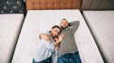 overhead view of smiling couple lying on bed in furniture store with arranged mattresses