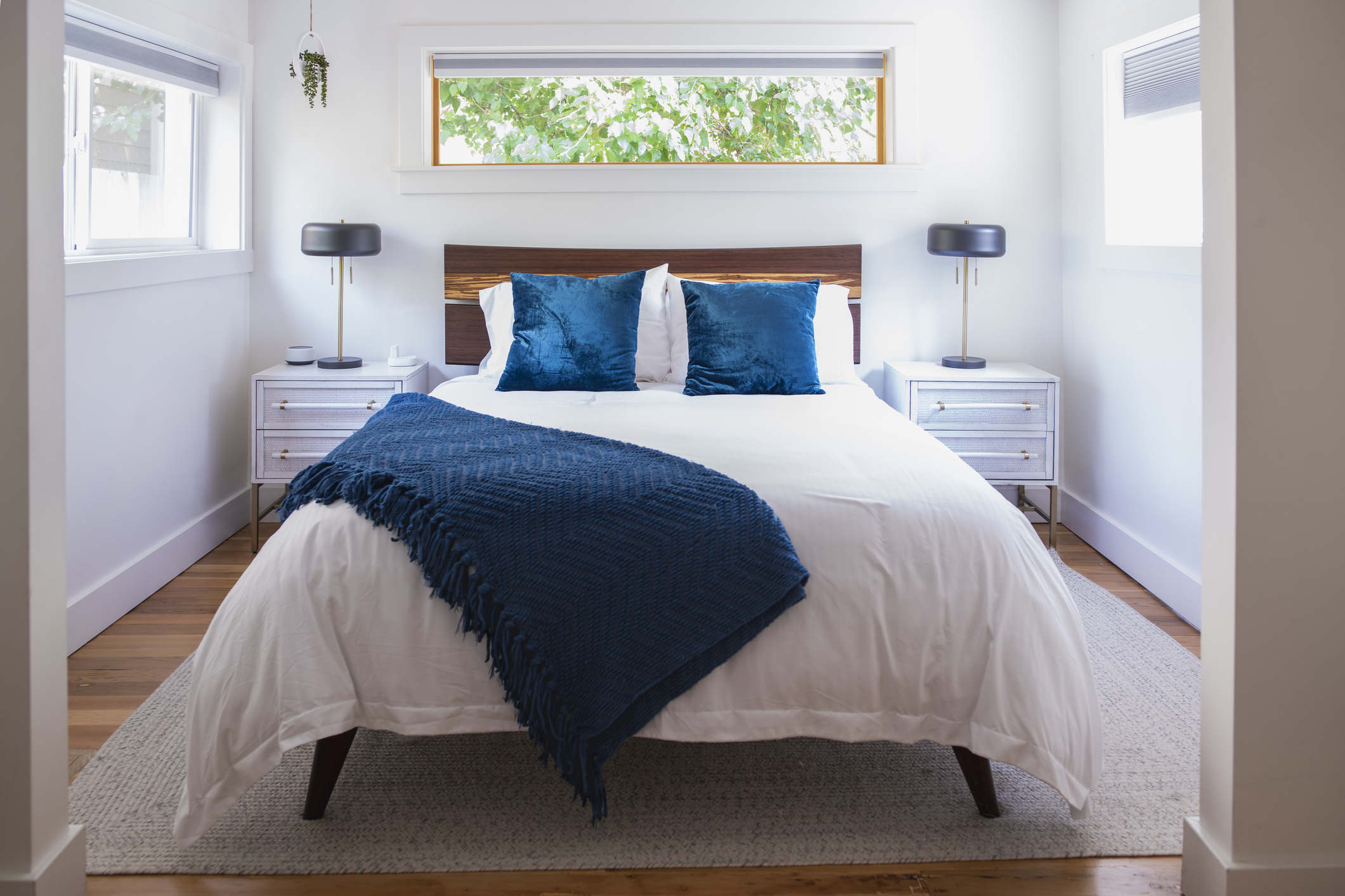 View of light, bright bedroom and double bed with white bedspread and blue pillows