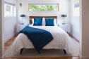 View of light, bright bedroom and double bed with white bedspread and blue pillows