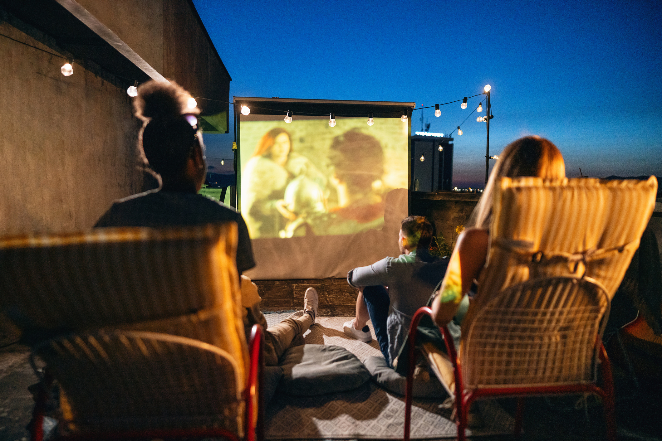 Group of unrecognizable multiracial young female and male friends, watching a movie on the rooftop