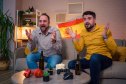 Two friends express excitement while watching a sports event at home, surrounded by snacks.