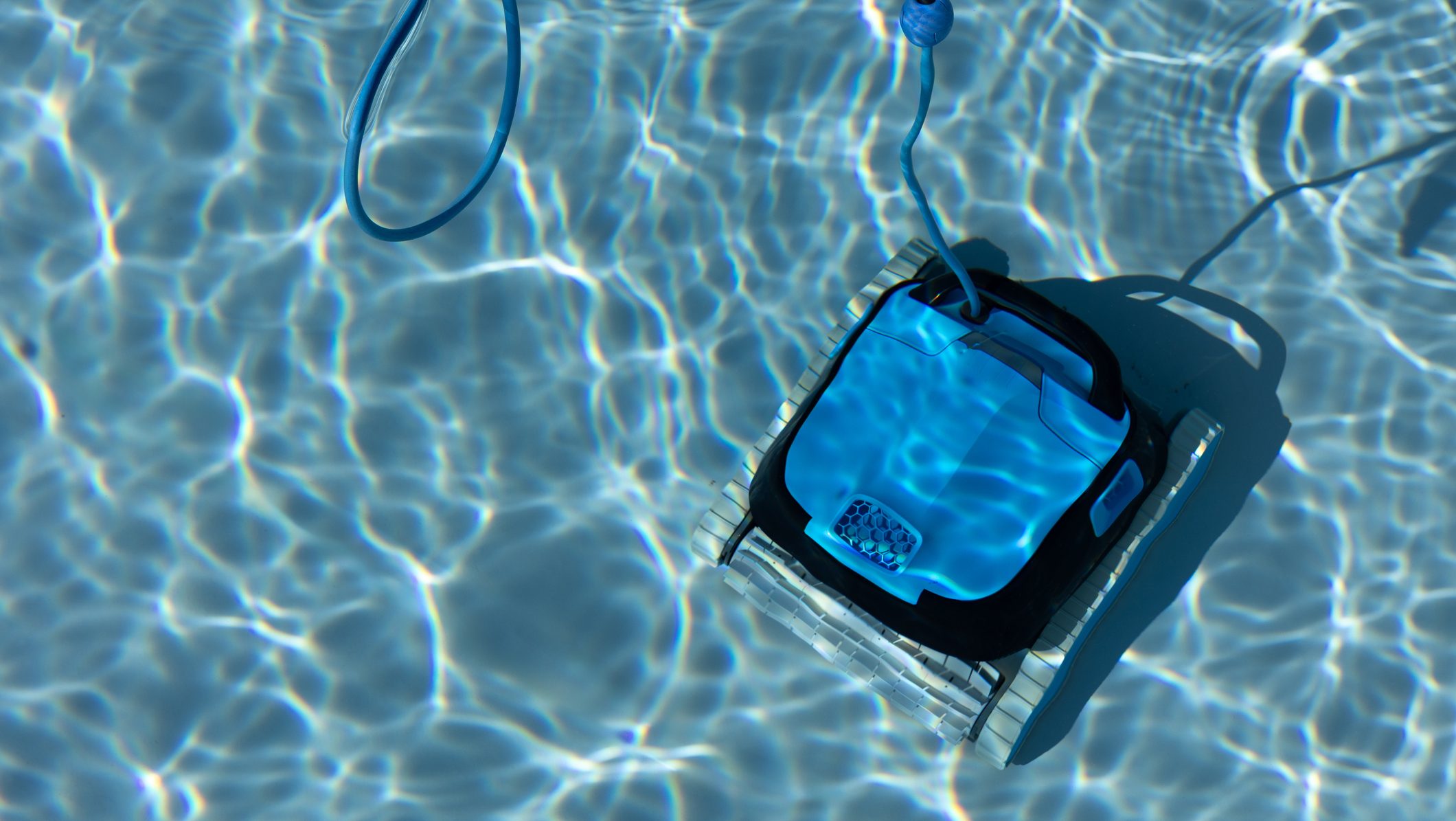 Robotic pool cleaner cleaning the bottom of a swimming pool with clear blue water and sunlight reflections, pool maintenance concept.