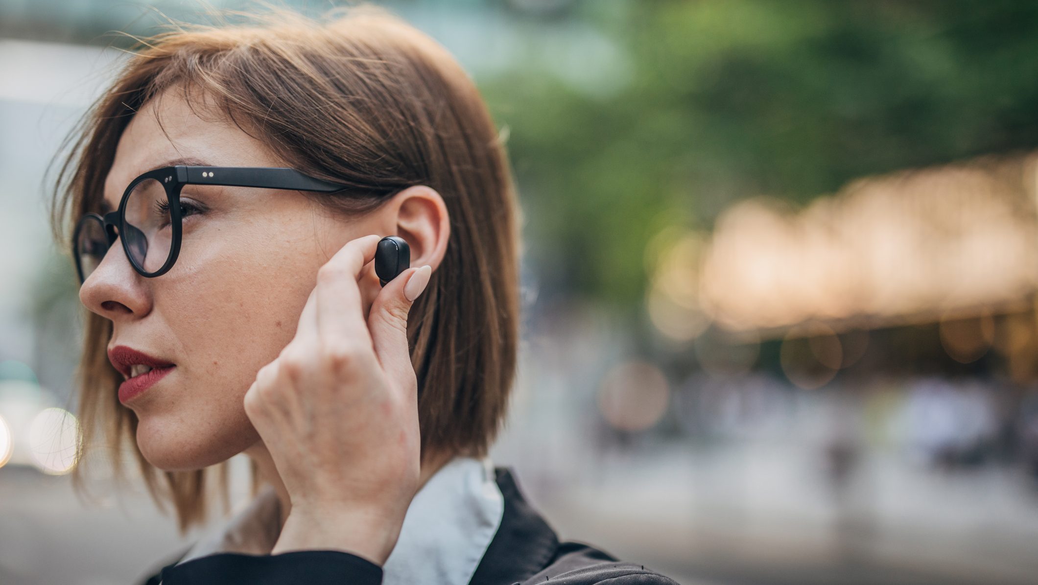 One woman, beautiful young businesswoman standing on the street downtown, using wireless headphones.