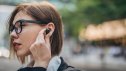 One woman, beautiful young businesswoman standing on the street downtown, using wireless headphones.