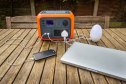 Portable power station solar electricity generator outdoors on wooden table with laptop, mobile phone and light electronic devices charging. Wireless charging lithium battery backup for use off grid.