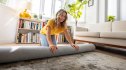 Happy Caucasian woman moving house and unrolling a carpet while unpacking - domestic life concepts
