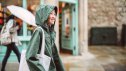 Cheerful teenage girl in raincoat walking under the rain while exploring in a town.