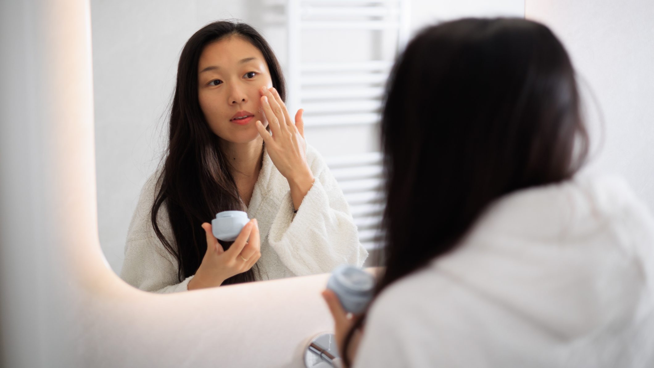 Beautiful young Asian woman looking at her in the mirror and taking care of her skin