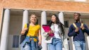 Three cheerful multiethnic students walking and chatting together on a sunny university campus, enjoying their education and friendships