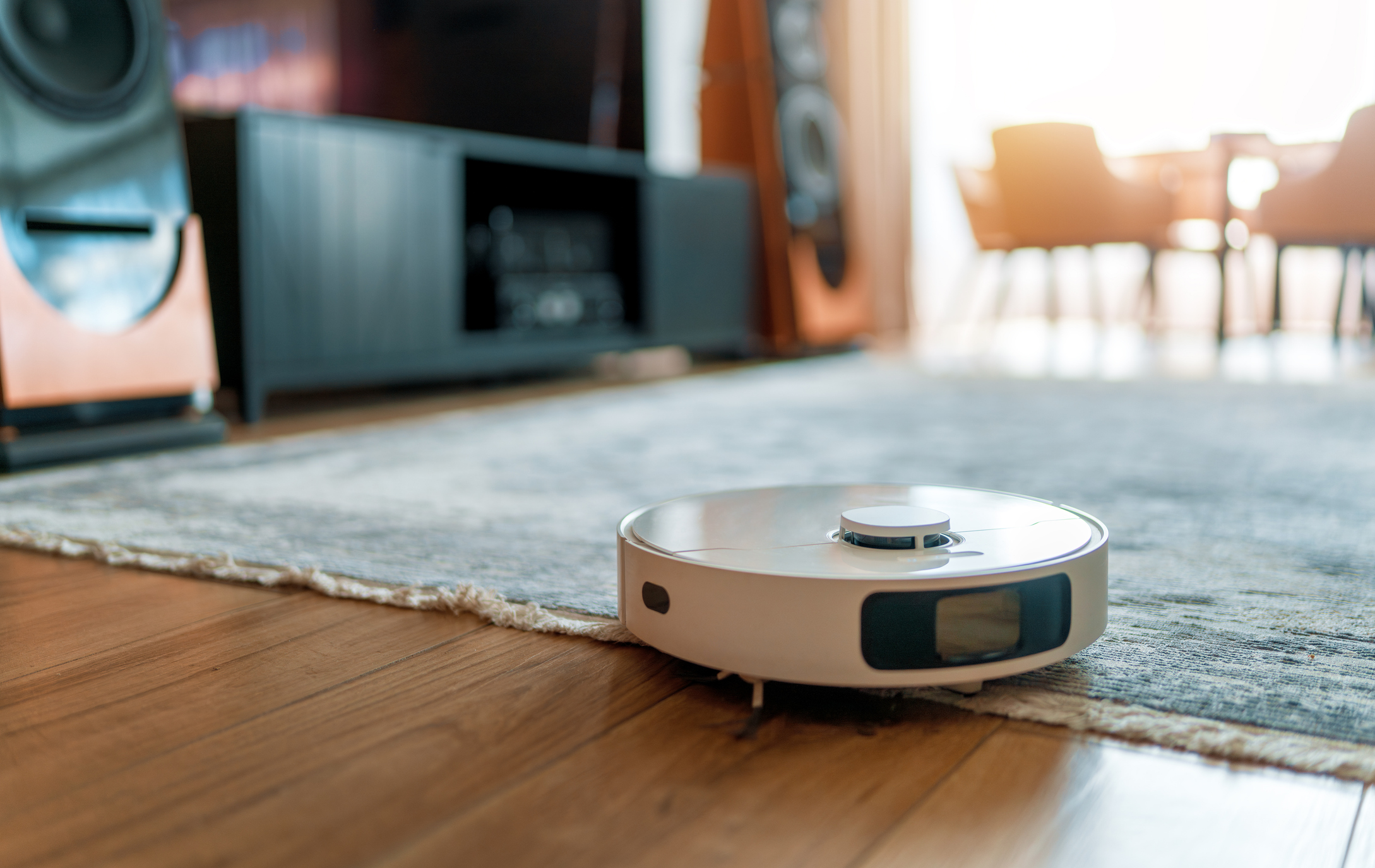 White robotic vacuum cleaner on wooden floor. Smart cleaning technology