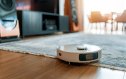 White robotic vacuum cleaner on wooden floor. Smart cleaning technology