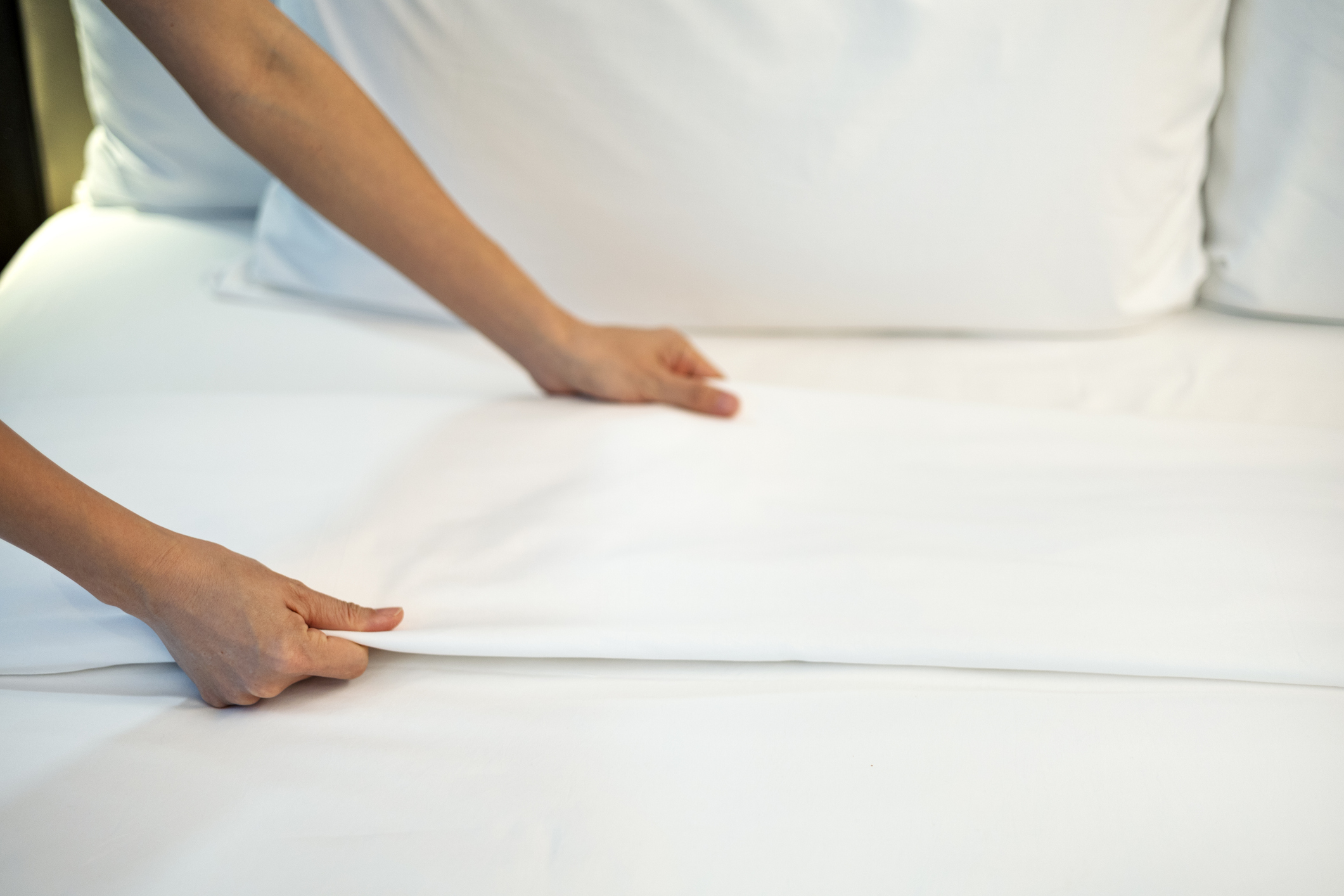 Close-up of a person adjusting clean white bed sheets on a neatly made bed, symbolizing comfort, cleanliness, and relaxation in a cozy home or hotel room environment.