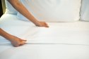 Close-up of a person adjusting clean white bed sheets on a neatly made bed, symbolizing comfort, cleanliness, and relaxation in a cozy home or hotel room environment.
