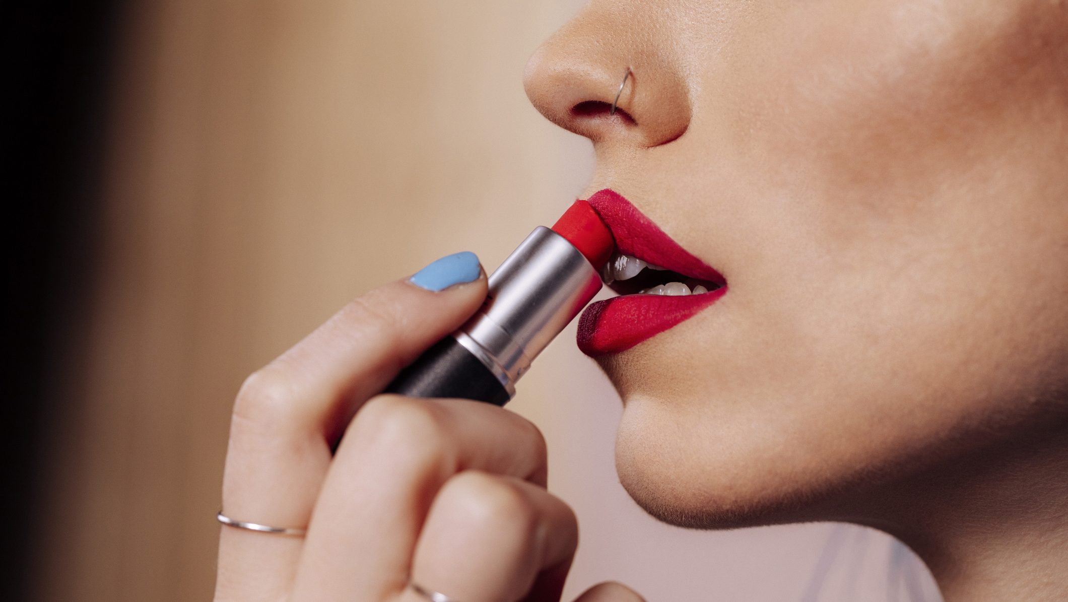 A detailed close-up of a woman applying vibrant red lipstick, showcasing glossy makeup, smooth skin, and a chic, stylish beauty moment suitable for fashion, cosmetics, and lifestyle campaigns