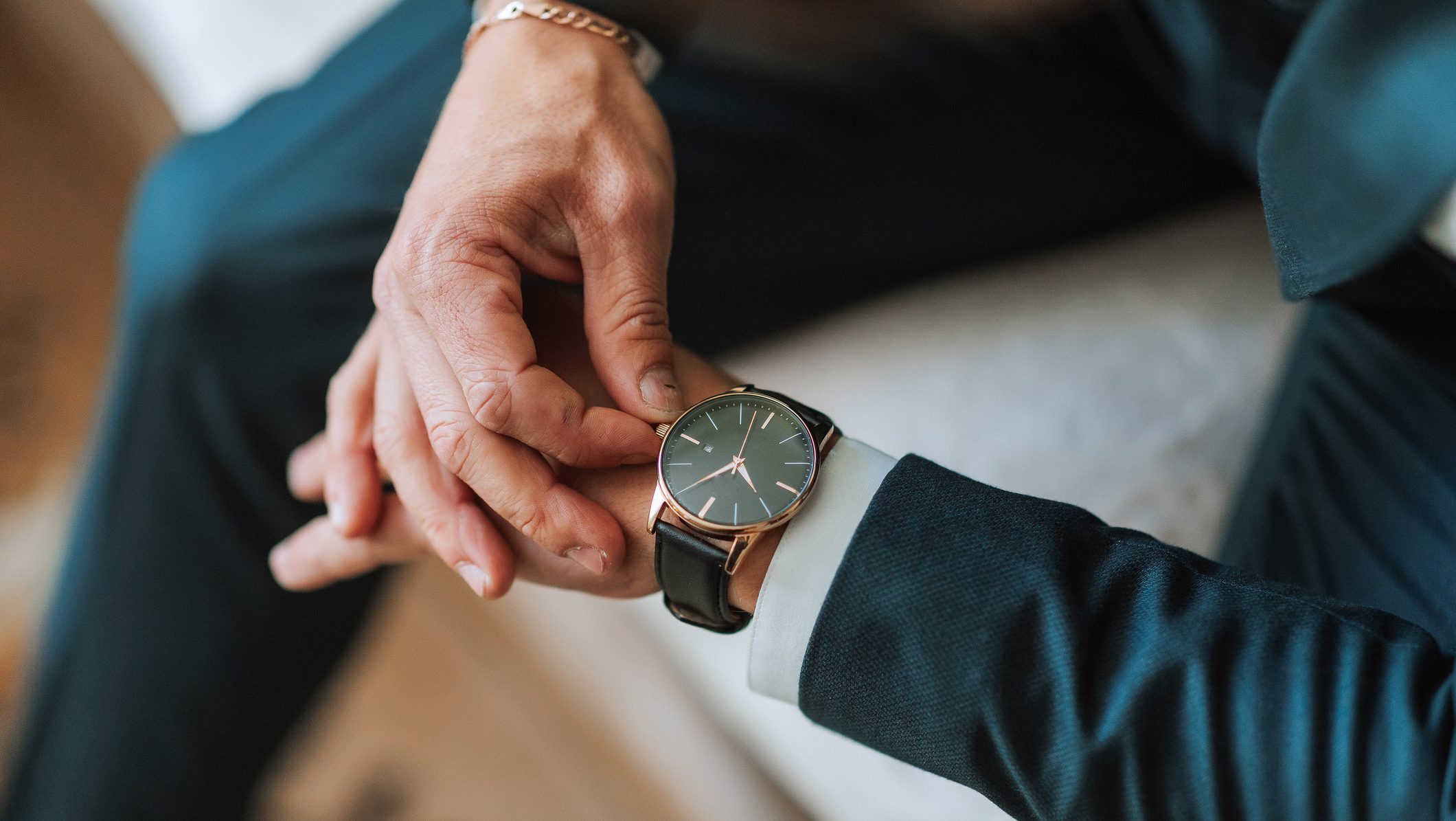 A man is wearing a watch and is looking at it. He is wearing a suit and tie