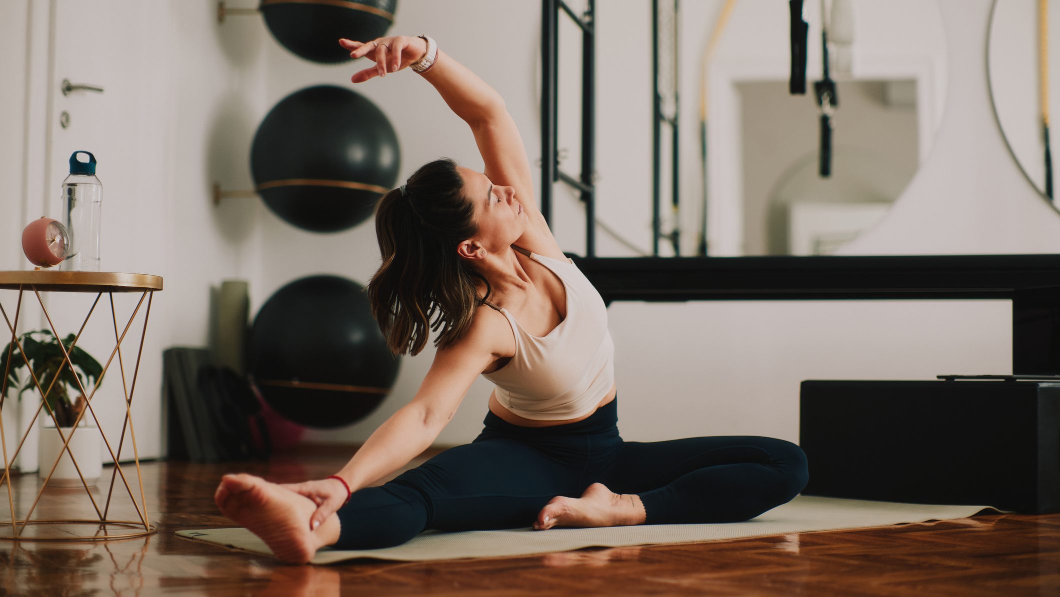 Middle-aged woman practicing pilates stretch on a mat in a bright fitness studio