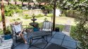 Young man lying down on patio lounge chair in outdoor spring flower garden in backyard porch of home happy smiling in zen with fountain, pergola canopy gazebo, table, plants, sofa