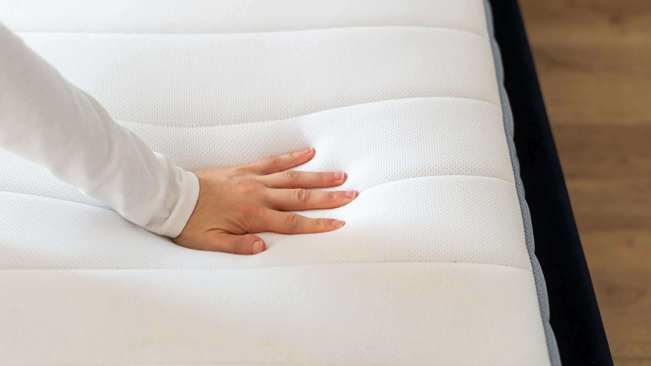 Cropped shot of woman hand testing new orthopedic memory foam core mattress at comfortable bed at home. Female customer choosing equipment for healthy sleeping