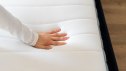 Cropped shot of woman hand testing new orthopedic memory foam core mattress at comfortable bed at home. Female customer choosing equipment for healthy sleeping
