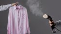 woman steaming pink shirt with hand steamer on hanger, close up