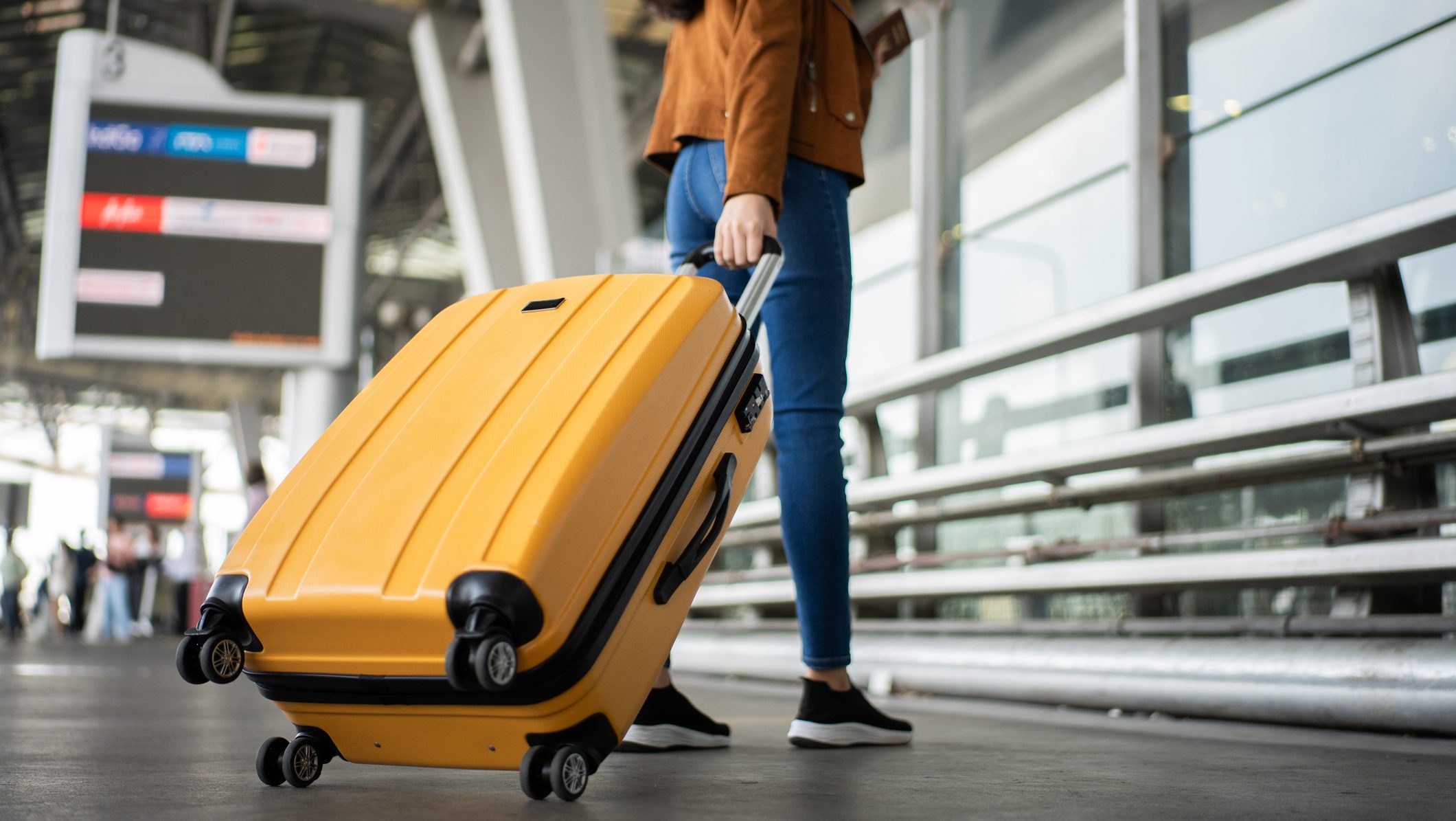 Close up of unrecognized woman tourist walking with her luggage through international airport terminal during holiday trip, female tourist rolling suitcase alone.