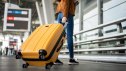 Close up of unrecognized woman tourist walking with her luggage through international airport terminal during holiday trip, female tourist rolling suitcase alone.