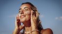 A happy young woman with sun-kissed skin applies sun cream to her face under a bright blue sky on a sunny beach in the Maldives
