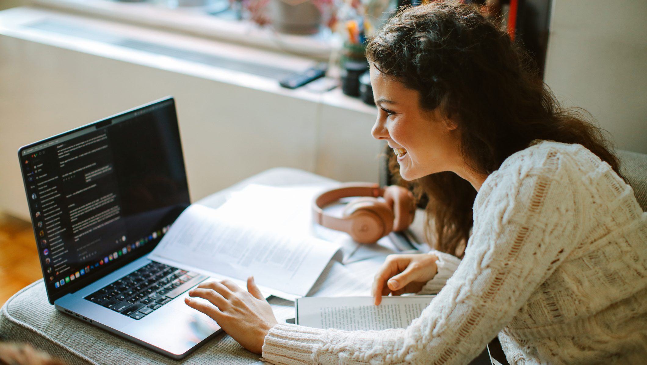 Female student focused on her studies at home, using a laptop and notes in a well-lit and modern apartment in New York.