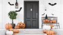 Carved pumpkins, bats and spiders on stairs and bench near modern house with black front door, tree in pot and white walls. Concept of halloween. 3d rendering