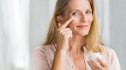 Smiling senior woman applying anti-aging lotion to remove dark circles under eyes. Happy mature woman using cosmetic cream to hide wrinkles below eyes. Lady using day moisturizer to counteract the aging of the skin.