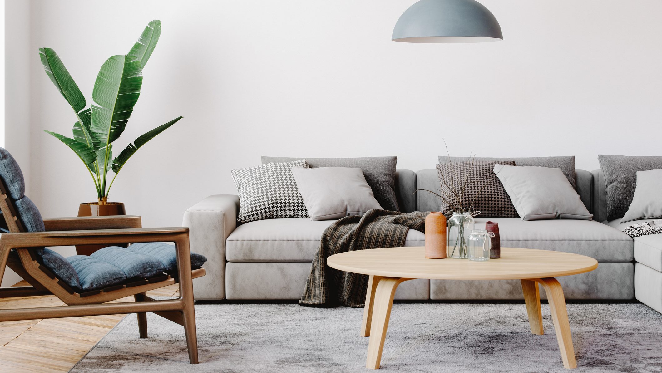 Modern living room setup with classic parquet floor. Furnished with light gray sofa, blue arm chair with wooden frame, modern blue ceiling lamp, wooden coffee table and gray carpet.